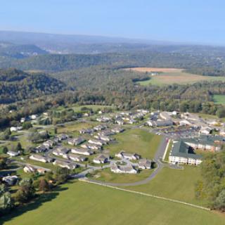 A panoramic aerial view of a rural community surrounded by lush hills and open fields.