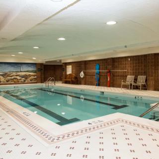 An indoor swimming pool with tiled flooring and walls, featuring lounge chairs and a mural.