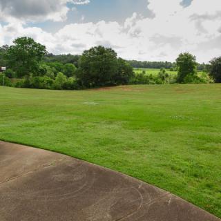 A scenic view of a lush green lawn bordered by trees under a partly cloudy sky.