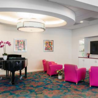 A modern lobby with pink chairs, a grand piano, and colorful artwork.