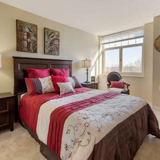 A cozy bedroom with a stylish red and brown bedding set, complemented by artwork and a large window letting in natural light.