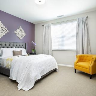 A modern bedroom with a purple accent wall, featuring a comfortable bed and a bright yellow chair.