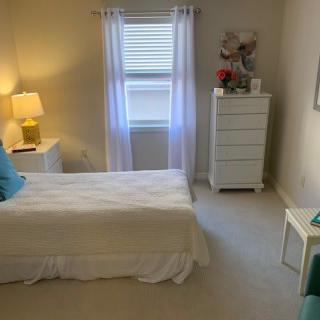 A neatly arranged bedroom with a bed, lamp, and dresser by the window.