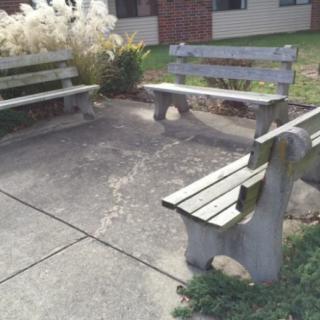 A small outdoor area with three concrete benches surrounding a paved space.