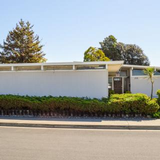 A modern, mid-century style home with a white exterior and surrounding greenery.