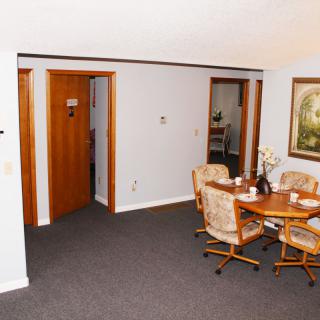 A cozy dining room with a round table and four chairs, adorned with wall art and carpeted flooring.