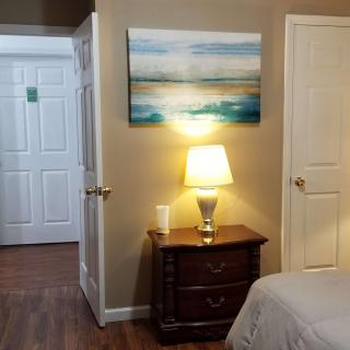 A cozy bedroom with a nightstand and lamp, featuring a painting above.