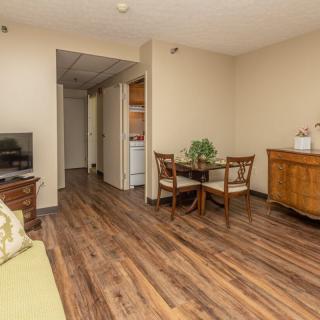 A cozy living and dining area with wood flooring, featuring a small dining table with chairs, a television, and additional furniture.
