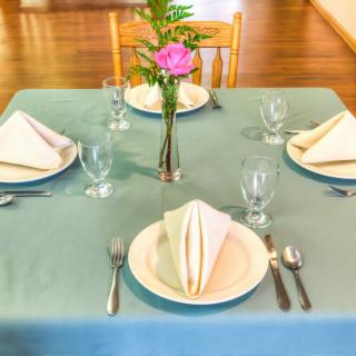 A neatly arranged dining table set for four, featuring folded napkins, glassware, and a floral centerpiece.
