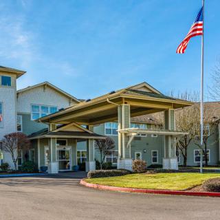 A large building with a covered entrance and a flagpole in front, surrounded by landscaping.