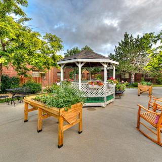 A serene outdoor garden featuring a gazebo, surrounded by trees and seating areas.