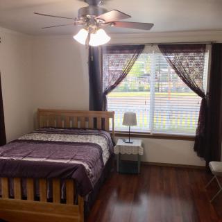 A cozy bedroom with a wooden bed, bedside lamp, and large window with curtains.