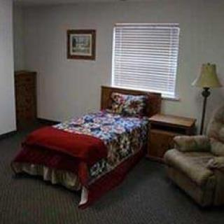 A small bedroom with a single bed, armchair, and nightstand next to a window.