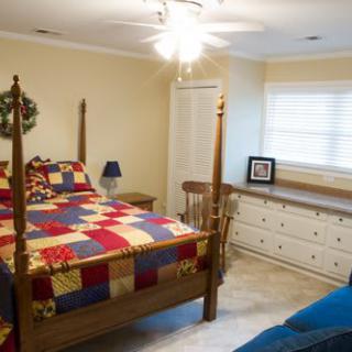 A cozy bedroom with a wooden bed and colorful quilt, alongside a dresser and table lamp.