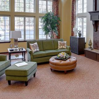 A cozy living room with green sofas, a brown ottoman, and large windows.