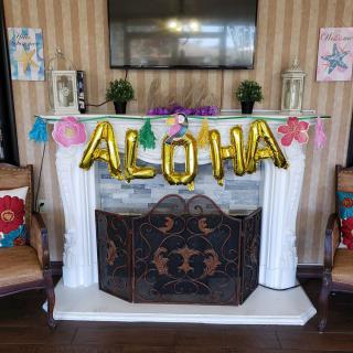 A fireplace decorated with 'ALOHA' balloons and tropical-themed decorations, setting a Hawaiian party atmosphere.
