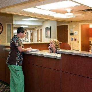 A nurse interacts with a receptionist at a hospital reception desk.