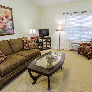 A cozy living room with a sofa, coffee table, and armchair, complemented by a TV and decorative elements.