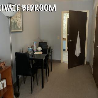 A cozy bedroom space featuring a small dining area, lamp, and open doorway.