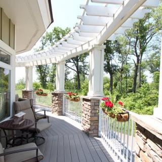 A sunny balcony with a pergola and potted plants, overlooking a lush green landscape.