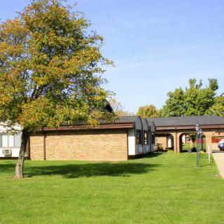A sunny day with a view of a building surrounded by green lawns and trees.