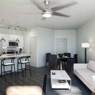 A modern open floor plan living room with a kitchen area, featuring contemporary furniture and a ceiling fan.