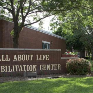 A view of the All About Life Rehabilitation Center with surrounding trees and landscaping.