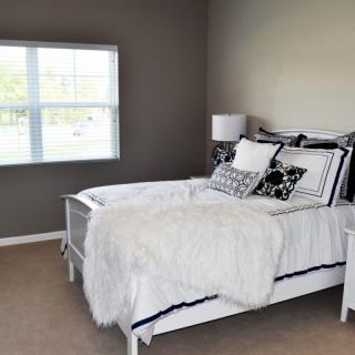 A cozy bedroom with neutral tones, featuring a bed with decorative pillows and a lamp by the window.