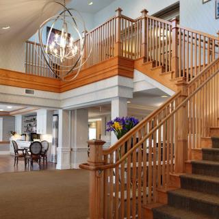 A spacious lobby with a wooden staircase and modern chandelier.