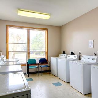 A clean and bright laundry room with several washing machines and dryers along with chairs by a large window.