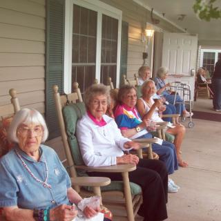 A group of elderly women sitting on a porch in rocking chairs, enjoying the outdoors.