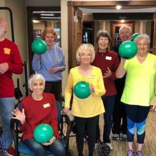 A group of seniors smiling and holding exercise balls in an indoor setting.