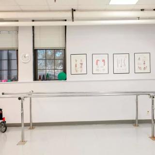An empty dance studio with a ballet barre and framed artwork on the wall.
