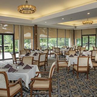 An elegant dining room with neatly arranged tables and chairs, featuring large windows and chandeliers.