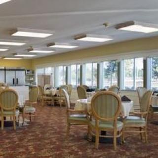 A spacious dining room with neatly arranged tables and chairs, featuring large windows providing natural light.