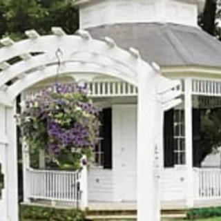 A white gazebo with a pergola and a hanging flower basket in a garden setting.