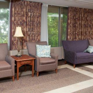 A cozy waiting area with chairs, a sofa, and lamps placed near large windows with drawn curtains.