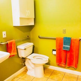 A brightly colored bathroom with green walls, featuring a toilet, sink, and orange towels.