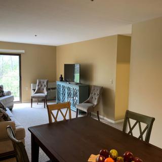 A cozy living and dining area with neutral tones, featuring a TV, seating, and a dining table.