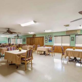 An empty dining room with tables and chairs, featuring ceiling fans and large windows.