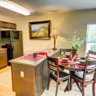 A cozy kitchen and dining area with a table set for four, featuring a modern design with wooden cabinets and bar stools.