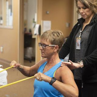 A person participating in physical therapy using resistance bands, guided by a therapist.