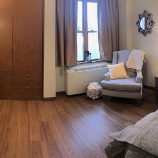 A cozy bedroom corner with a comfortable chair, soft lighting, and wooden floors.
