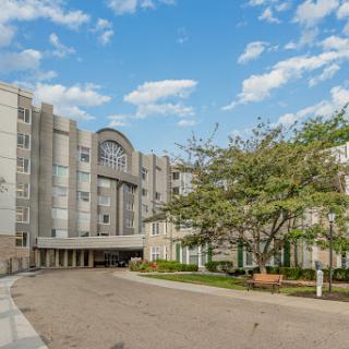 A modern multi-story building surrounded by greenery under a bright blue sky.