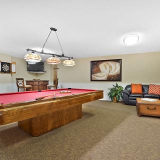 A cozy billiard room with a red-felt pool table and comfortable seating, accentuated by warm lighting and decorative artwork.