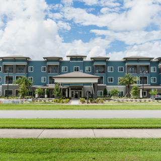 A modern hotel building with a landscaped lawn and a clear sky in the background.