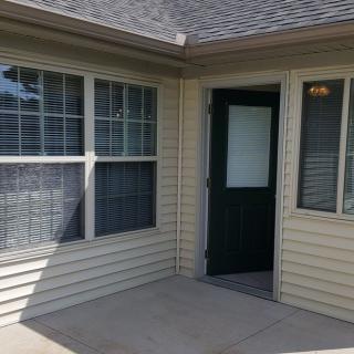 A small patio area featuring a dark green door and several large windows.