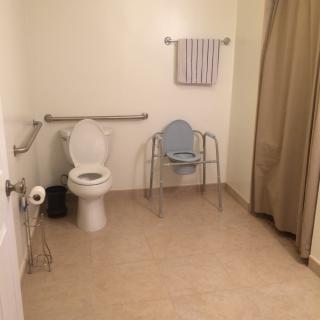A spacious, accessible bathroom with a toilet, grab bar, and shower chair.