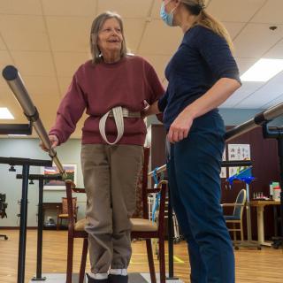 An elderly woman receives assistance from a healthcare professional during a physical therapy session.