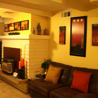 A cozy living room with warm lighting, featuring a sofa, fireplace, and various artworks on the walls.